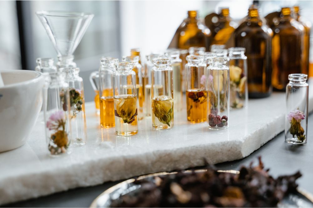 Vasitos con distintos aceites esenciales herbales y hierbas frescas sobre una base de madera – aromaterapia natural