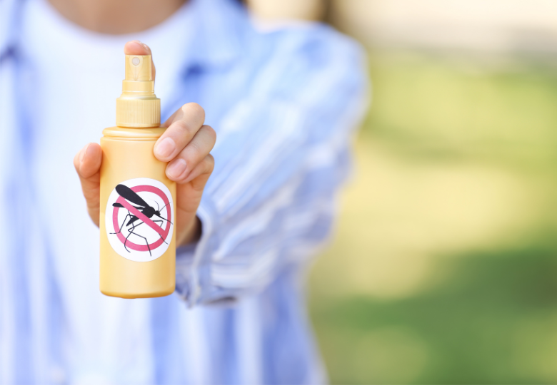 Persona sosteniendo un spray repelente contra mosquitos al aire libre.